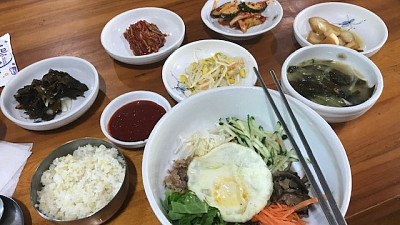 Tradiční korejský způsob stolování, kdy dostanete jedno hlavní jídlo – zde bibimbap (miska s rýží, chilli pastou, zeleninou a vajíčkem) – a pak hromadu malých porcí dobrot na zakusování, které se jmenují pančchan a jejich konzumace je na účet podniku. Zdroj: Andrea Annie Kubiňanová, se souhlasem
