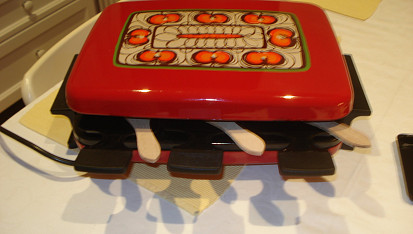 Raclette, Do něj se vkládají takové lopatky a na nich sýr. Dřevěné vařečky slouží k tomu odlepit ten sýr z lopatičky.