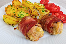 Válečky z mletého kuřecího masa obalené slaninou a pečené brambory s česnekem.