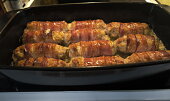 Válečky z mletého kuřecího masa obalené slaninou a pečené brambory s česnekem.