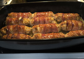 Válečky z mletého kuřecího masa obalené slaninou a pečené brambory s česnekem.