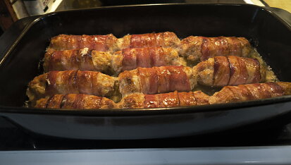 Válečky z mletého kuřecího masa obalené slaninou a pečené brambory s česnekem.