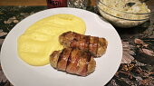 Válečky z mletého kuřecího masa obalené slaninou a pečené brambory s česnekem.