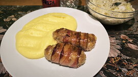 Válečky z mletého kuřecího masa obalené slaninou a pečené brambory s česnekem.