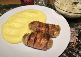 Válečky z mletého kuřecího masa obalené slaninou a pečené brambory s česnekem.